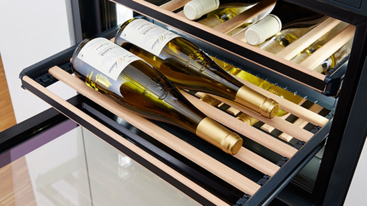 Zwei liegende Weinflaschen mit goldfarbenen Kapseln in einem modernen Weinkühlschrank mit Holzablagen in Ihrem Chalet in Wagrain