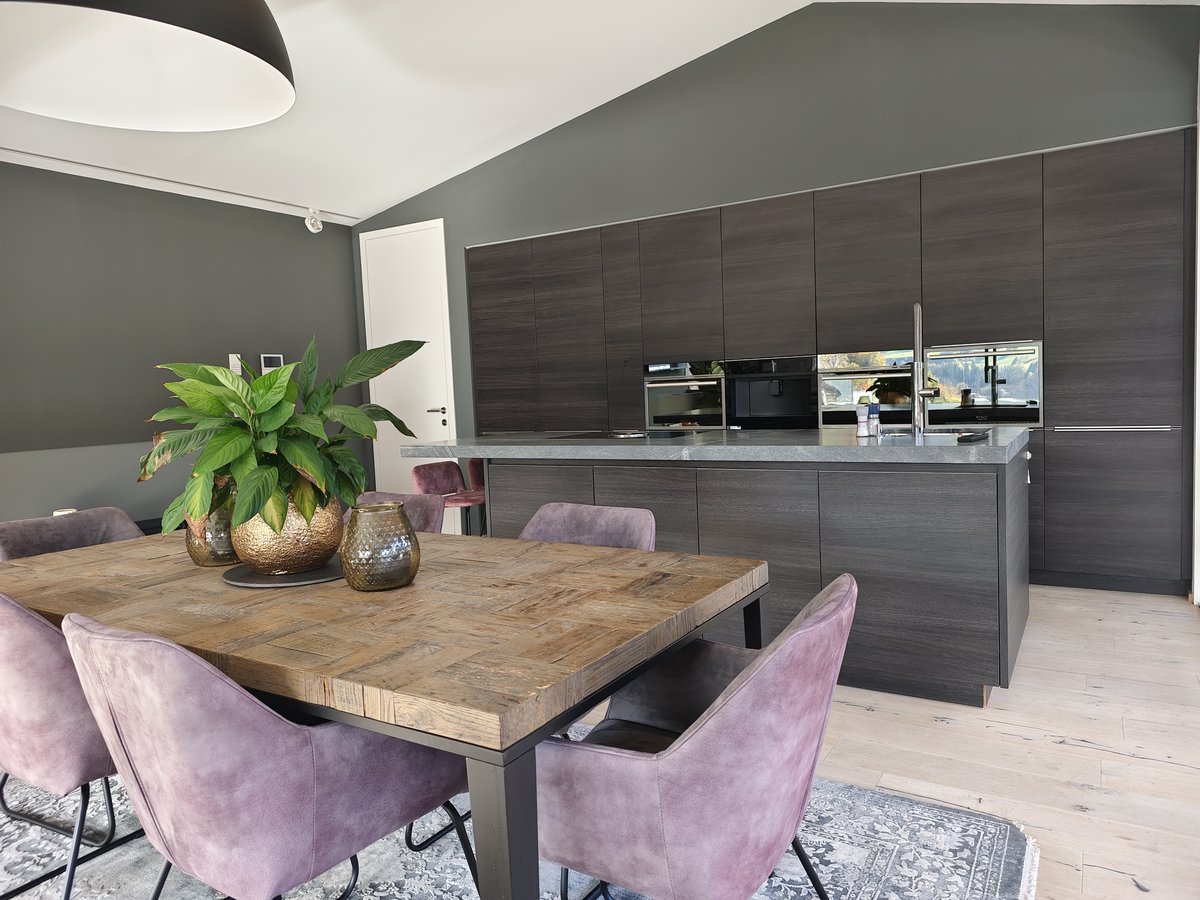 Moderne Küche mit dunklen Holzfronten, Kücheninsel mit Marmorarbeitsplatte, Holztisch und sechs violetten Samtstühlen auf gemustertem Teppich.